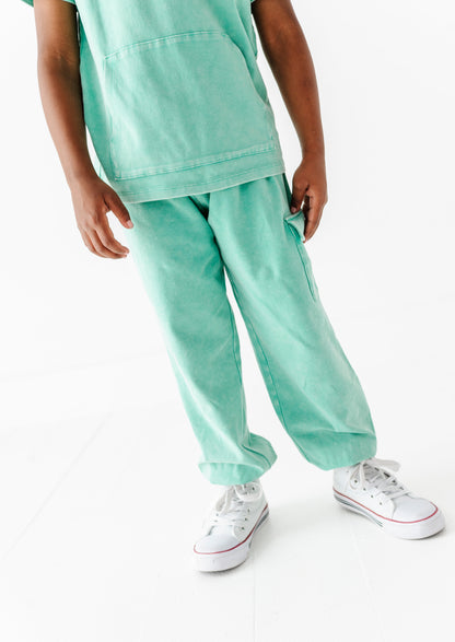 Child wearing a light green outfit with white sneakers on a white background