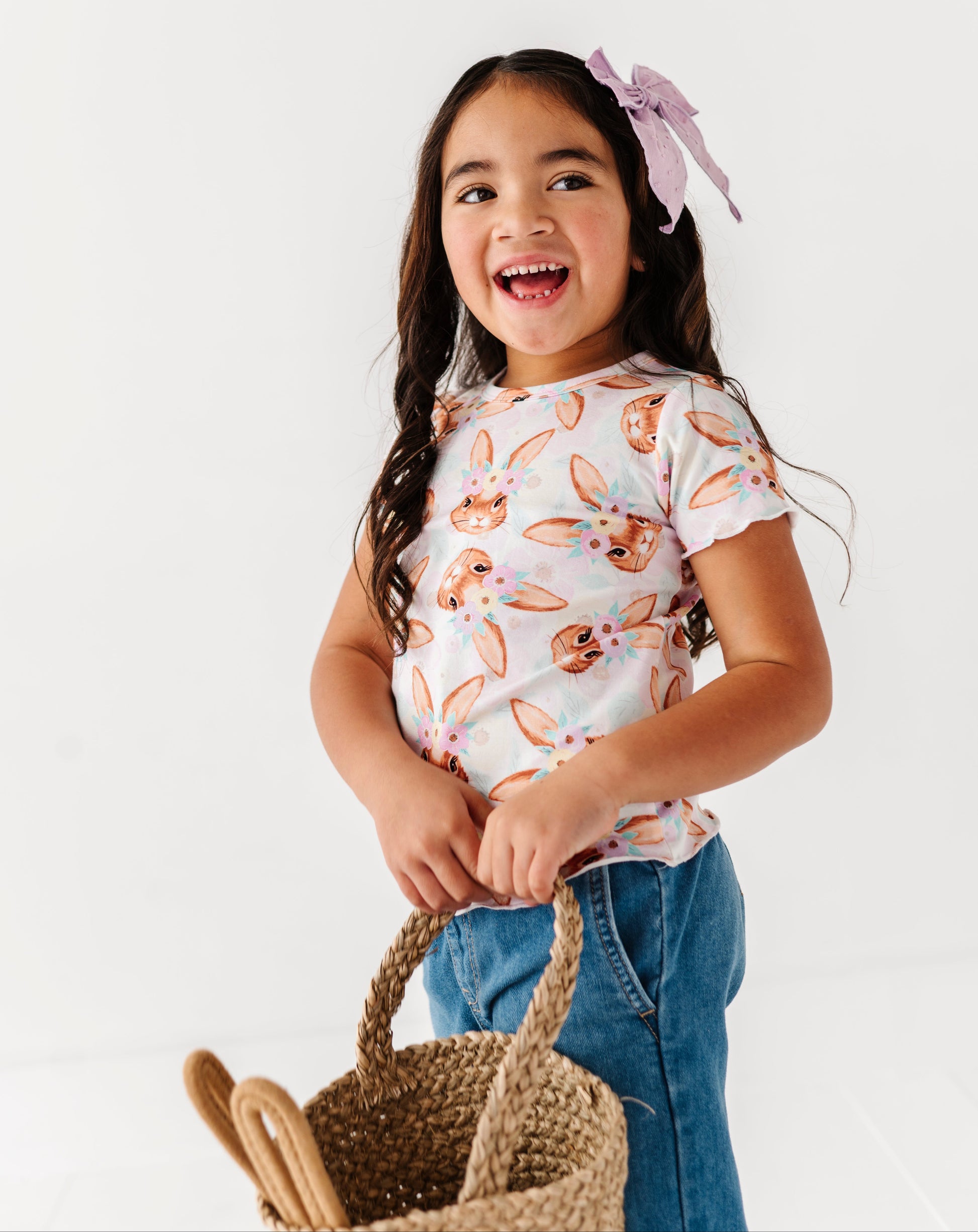 Young girl wearing a patterned shirt and holding a basket on a white background