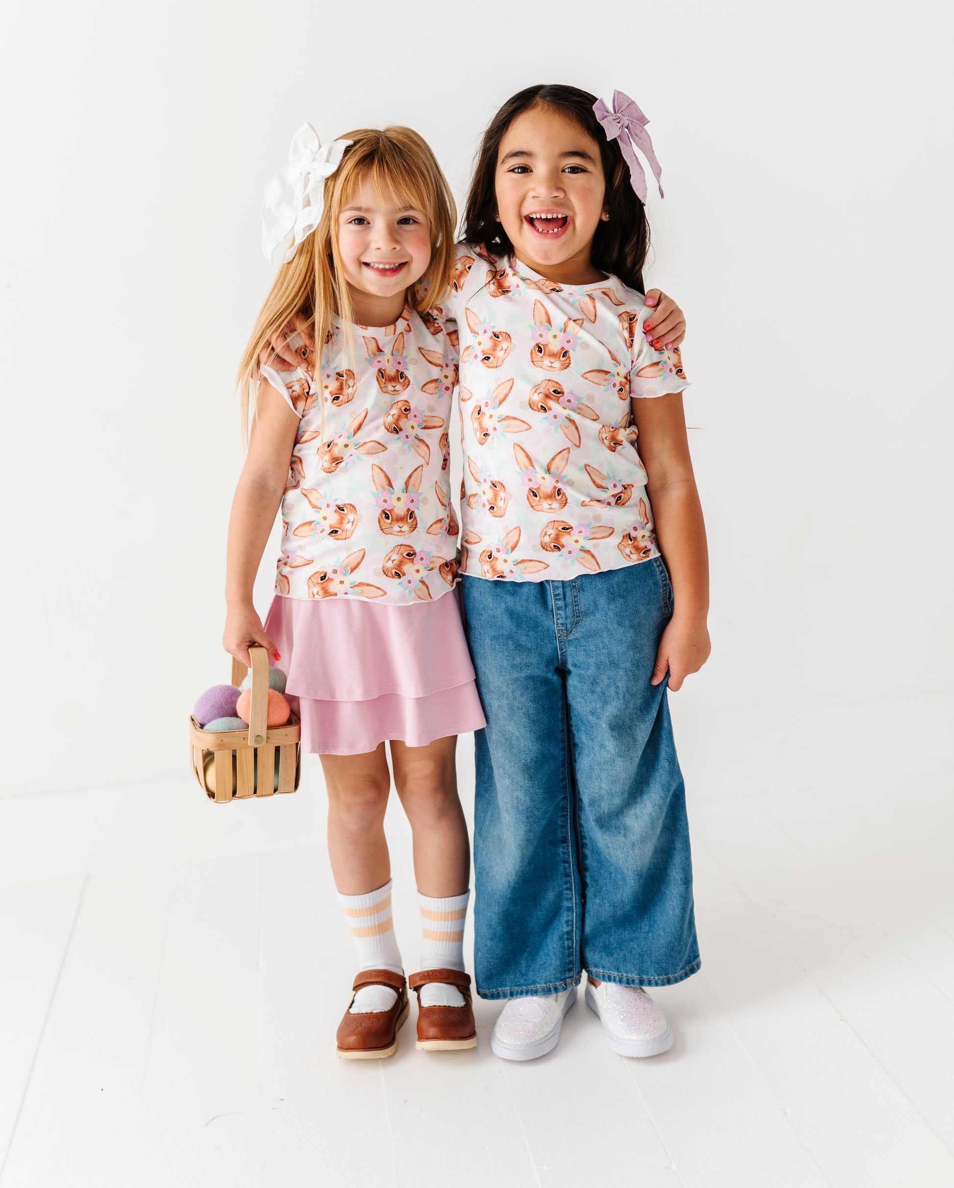 Two children wearing matching Easter bunny tops and skirts on a white background