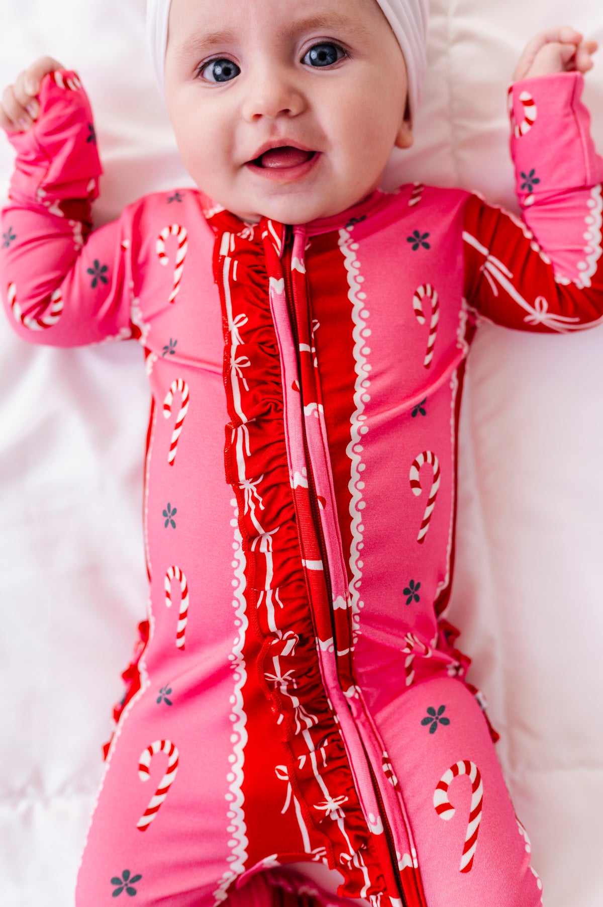 A baby girl wearing a red-and-pink bamboo Christmas convertible romper featuring ruffle detailing and foldover cuffs 