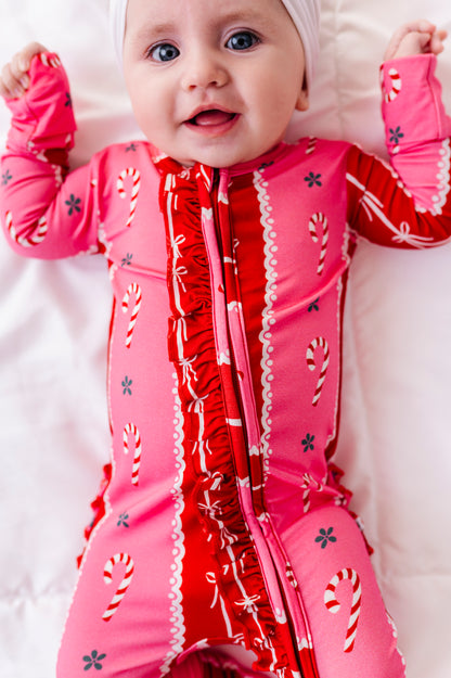 A baby girl wearing a red-and-pink bamboo Christmas convertible romper featuring ruffle detailing and foldover cuffs 