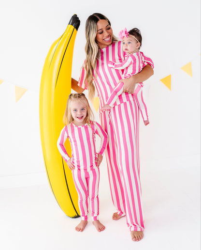 A woman and two young girls wearing matching pink and white vertically striped long-sleeve pajamas pose together in a studio setting. The woman holds a baby girl wearing a matching pink headband.