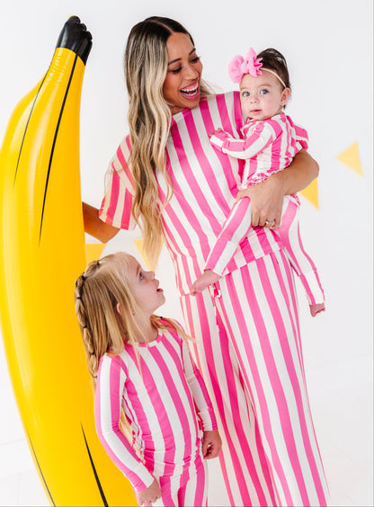 A woman and two children wearing matching pink and white striped one-piece outfits pose with a giant yellow inflatable banana prop against a white studio background.
