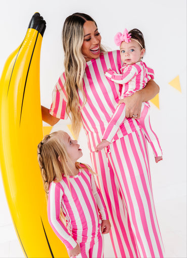 A woman and two children wearing matching pink and white striped one-piece outfits pose with a giant yellow inflatable banana prop against a white studio background.