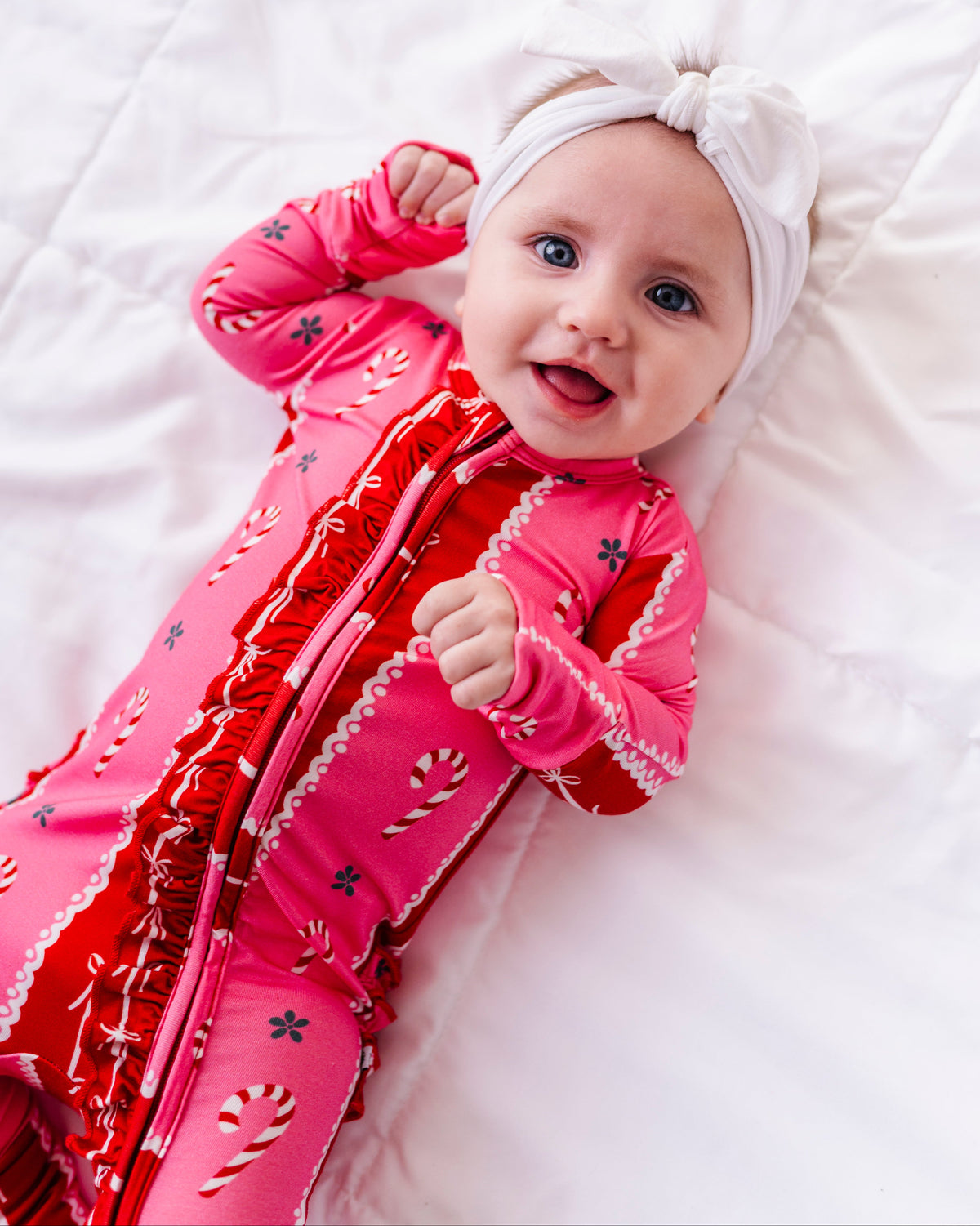 A baby girl wearing a red-and-pink bamboo Christmas convertible romper featuring ruffle detailing and foldover cuffs 