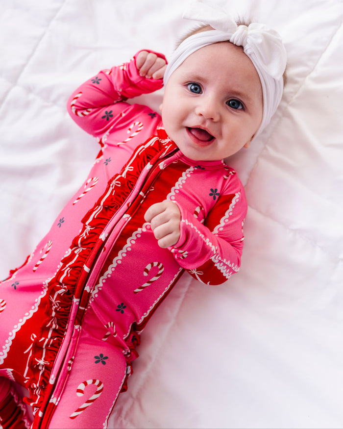 A baby girl wearing a red-and-pink bamboo Christmas convertible romper featuring ruffle detailing and foldover cuffs 