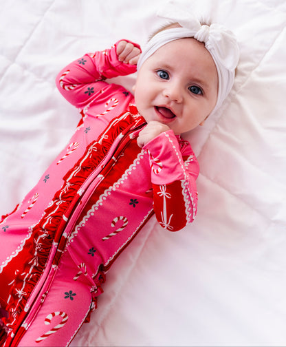 A baby girl wearing a red-and-pink bamboo Christmas convertible romper featuring ruffle detailing and foldover cuffs 