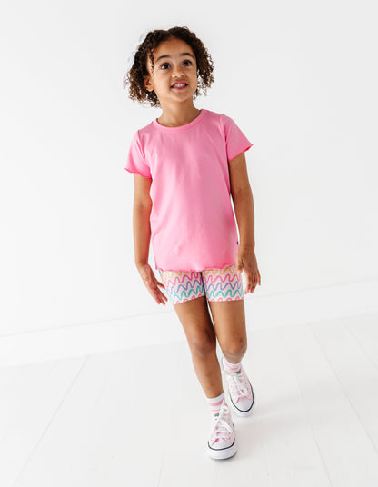 Child wearing a pink bamboo/cotton t-shirt and patterned bamboo biker shorts on a white background