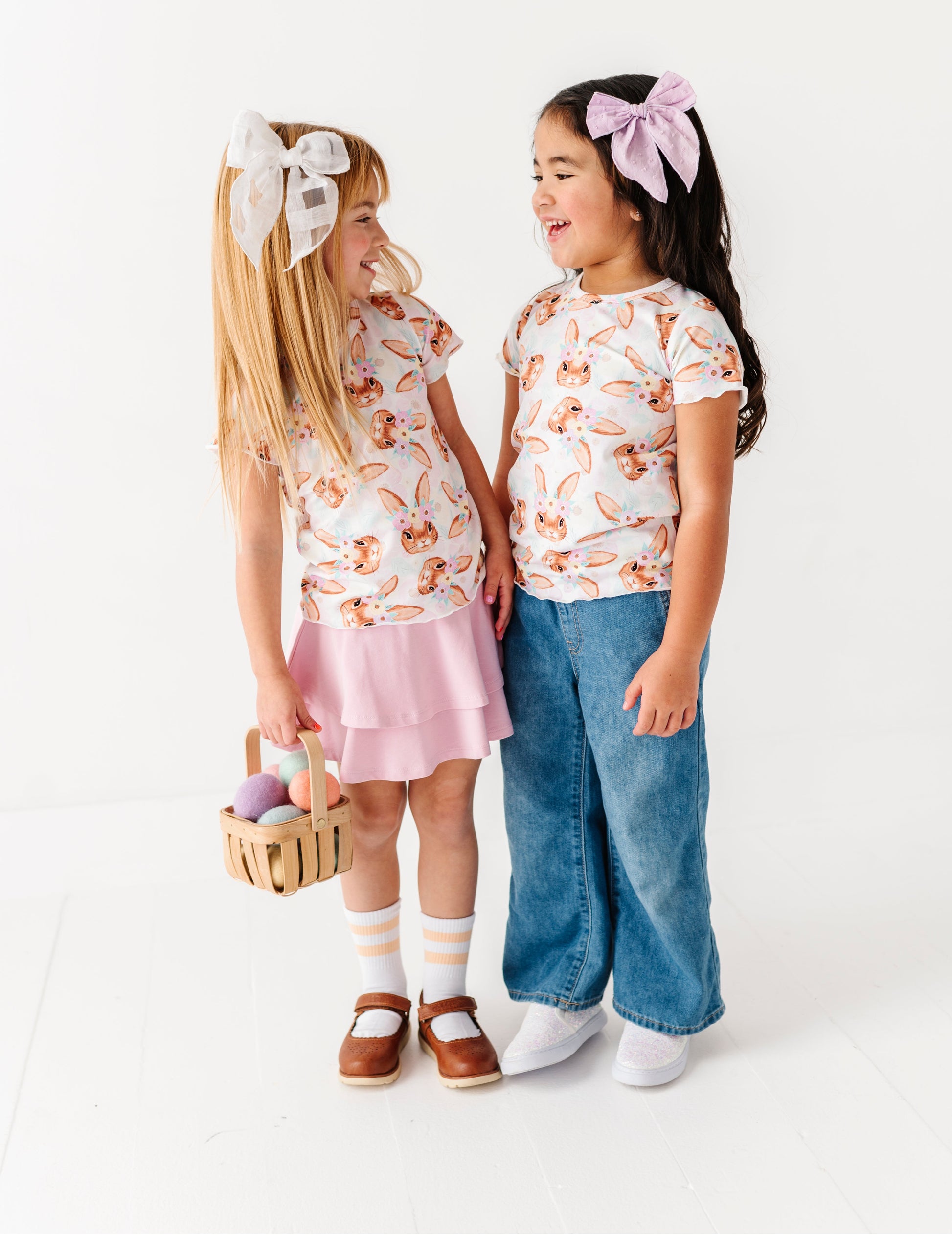 Two young girls wearing matching outfits with floral tops and pink skirts on a white background
