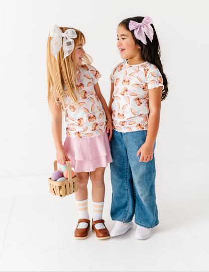 Two young girls wearing matching outfits with floral tops and pink skirts on a white background