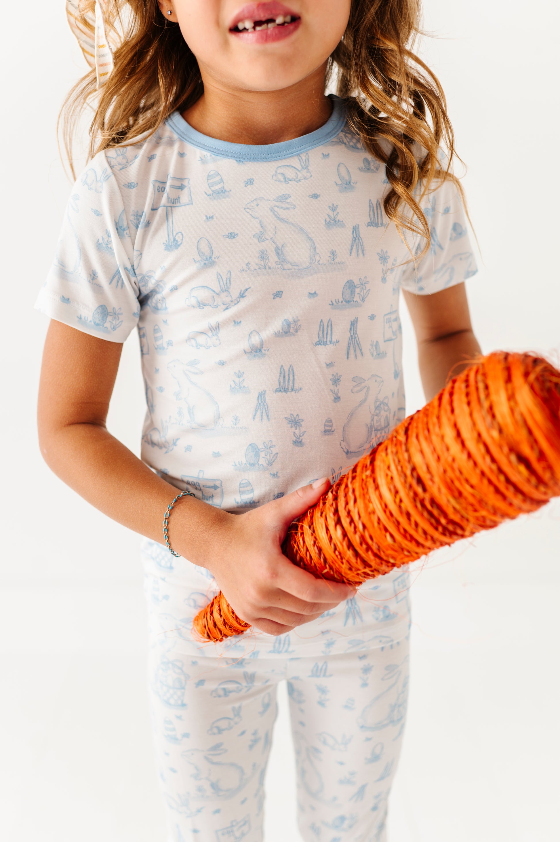 Child wearing a patterned shirt and pants holding an orange object against a white background