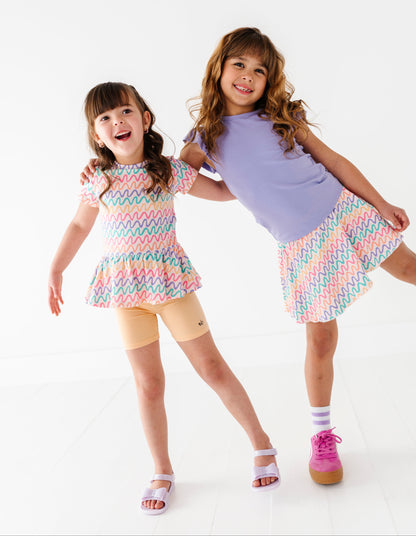Two young girls wearing colorful squiggly bamboo/cotton  outfits posing against a white background