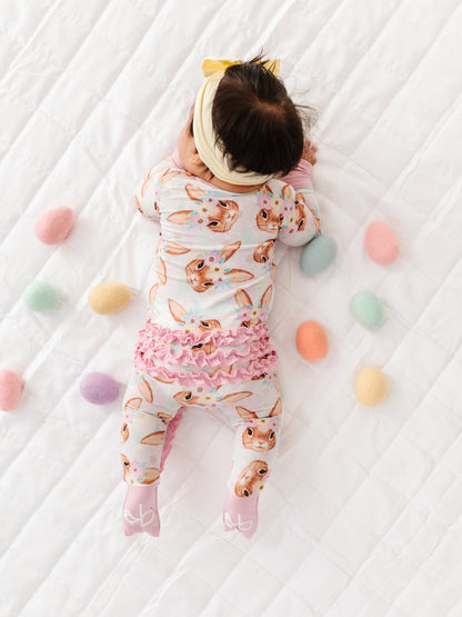 Baby lying on a white blanket with colorful eggs around, wearing a bunny bamboo romper.