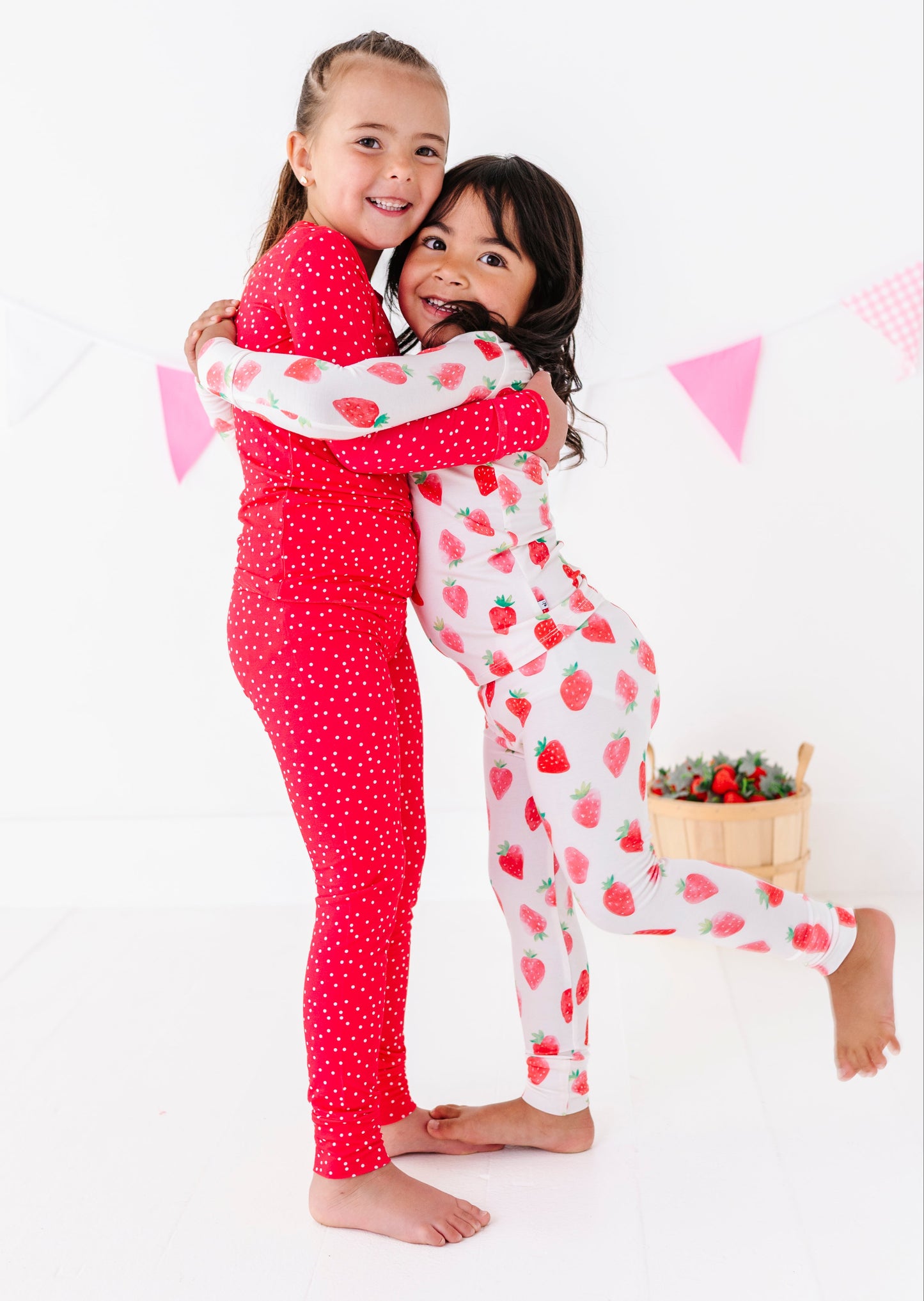 Two children in matching pajamas hugging on a white background with pink flags.