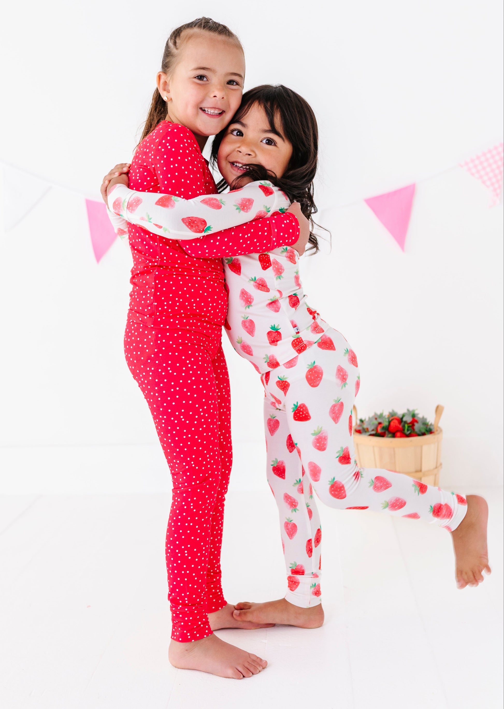 Two children in matching pajamas hugging on a white background with pink flags.