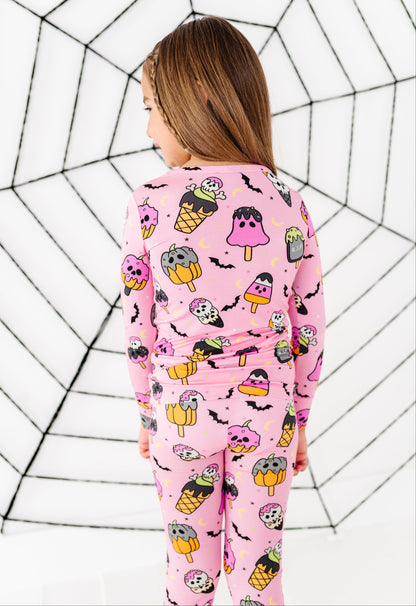 A child wearing a pink long-sleeve pajama set with a Halloween-themed ice cream cone print, shown from the back against a white background with a black spiderweb pattern.