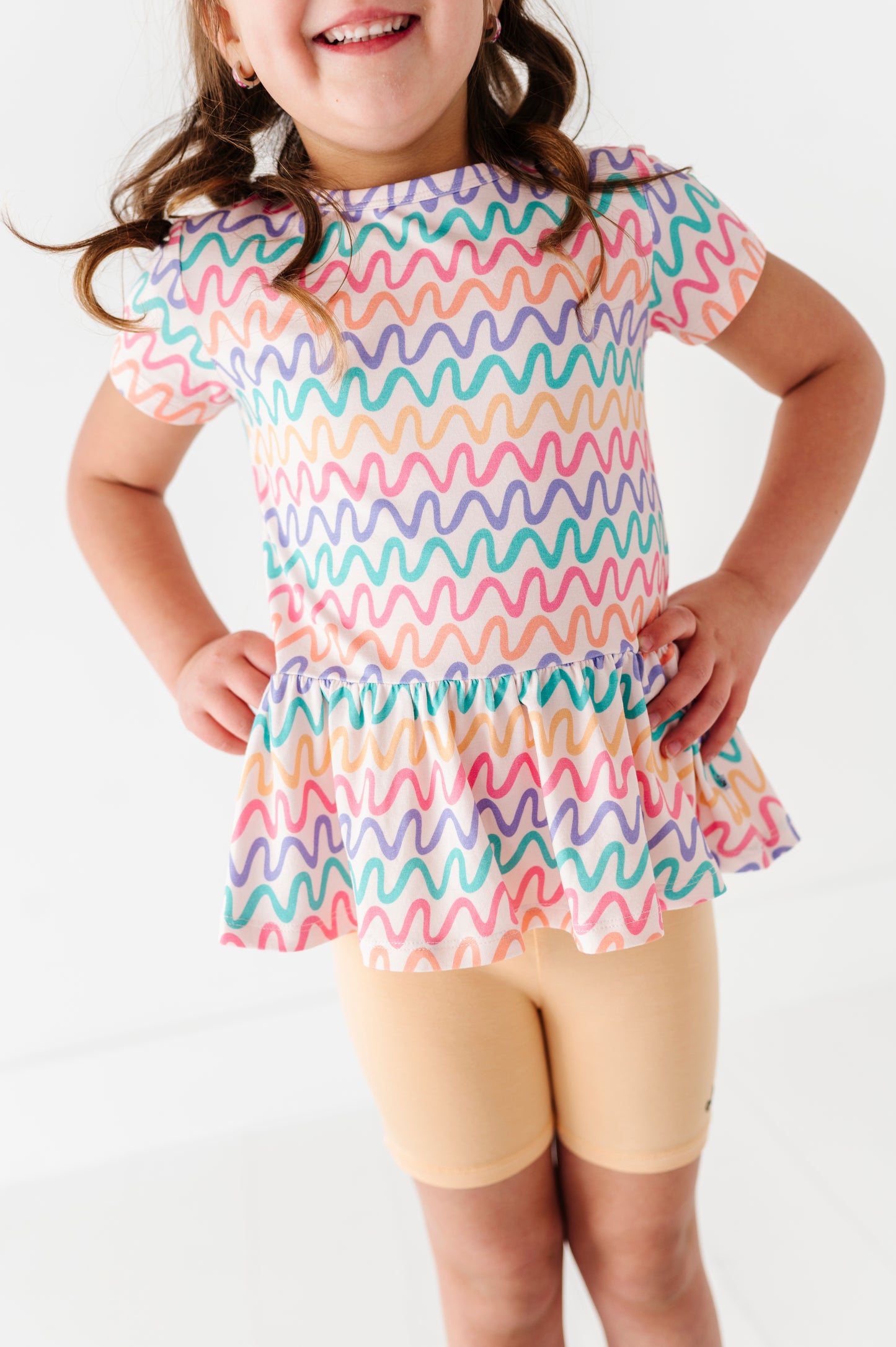 Child wearing a colorful wavy patterned bamboo/cotton peplum top and bamboo butter yellow biker shorts on a white background