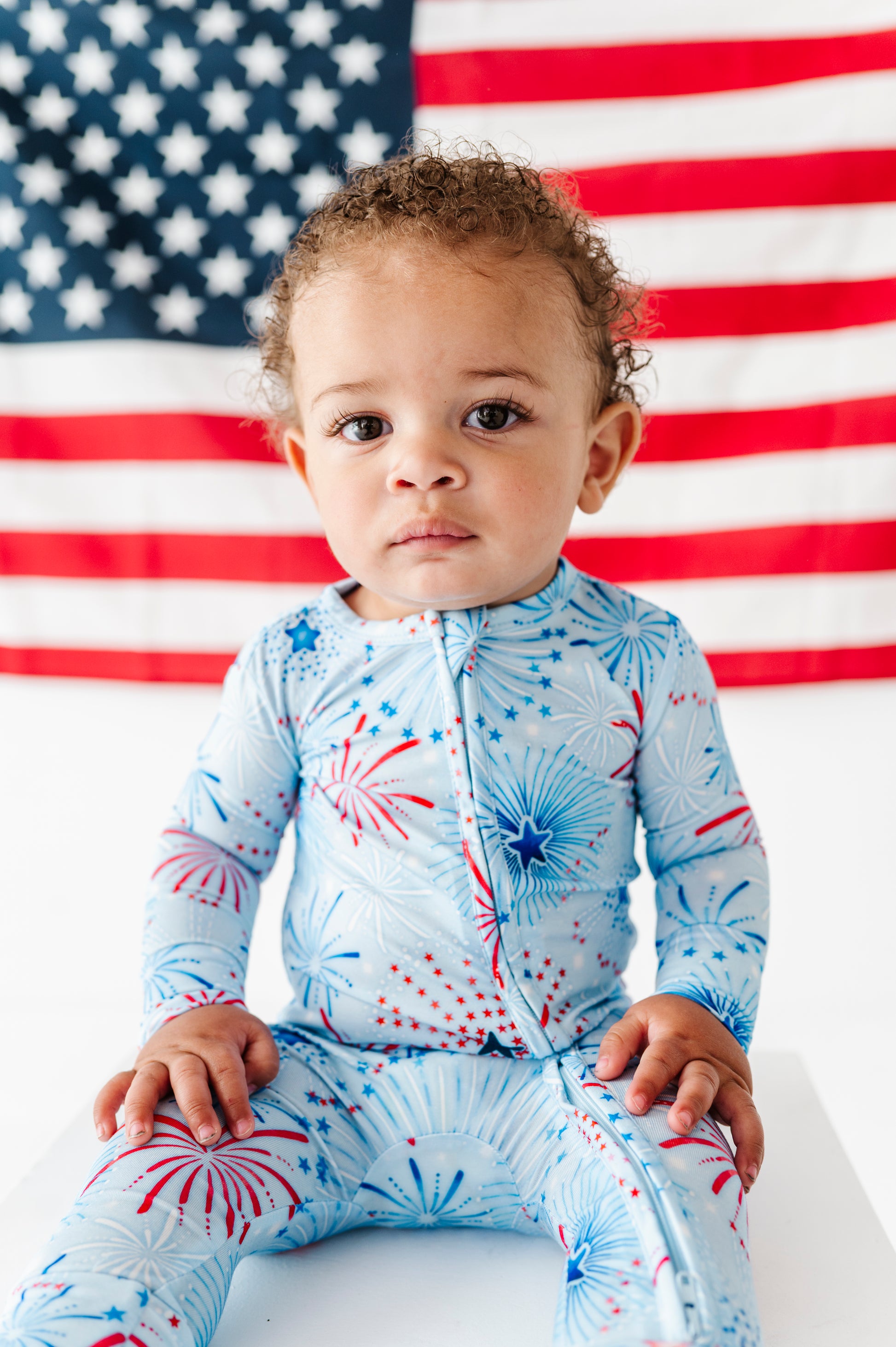 Child wearing a firework-themed bamboo onesie in front of an American flag