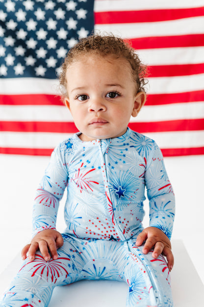 Child wearing a firework-themed bamboo onesie in front of an American flag