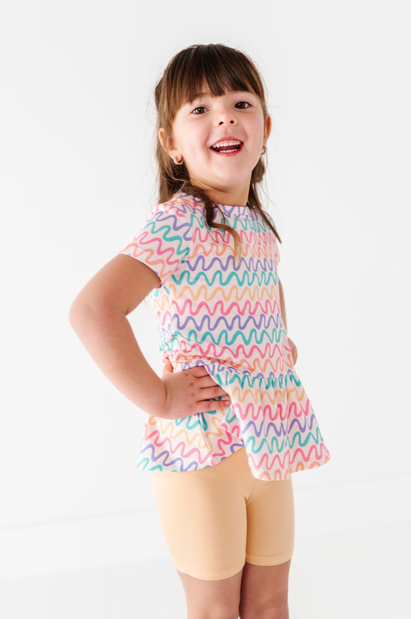 Child wearing a colorful bamboo/cotton peplum top and yellow bamboo biker shorts on a white background