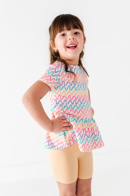 Child wearing a colorful bamboo/cotton peplum top and yellow bamboo biker shorts on a white background