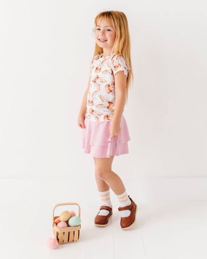 Young girl in a floral top and pink skirt holding a basket of Easter eggs on a white background