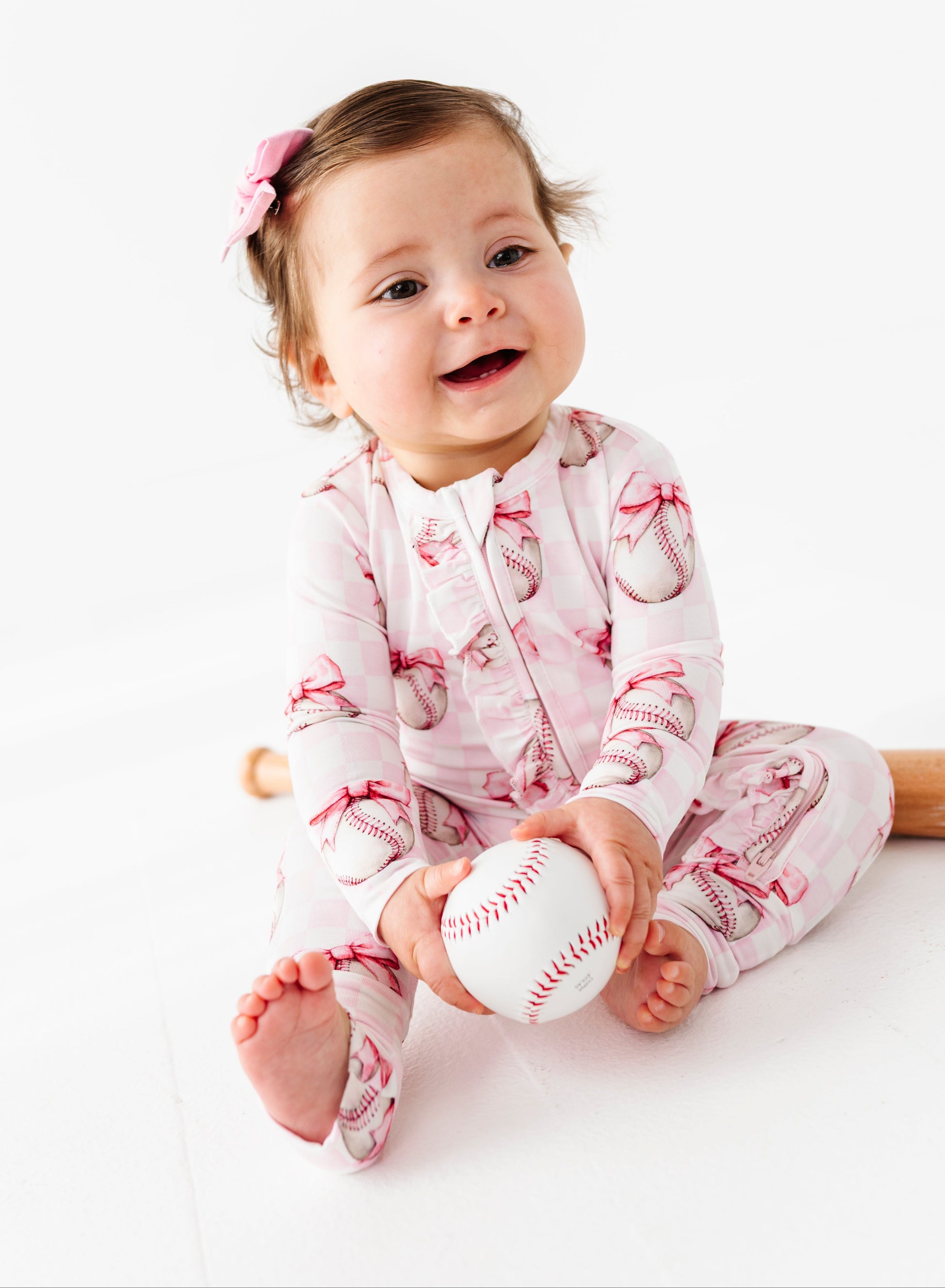Baby wearing a pink romper with a baseball design, holding a small white ball on a white background