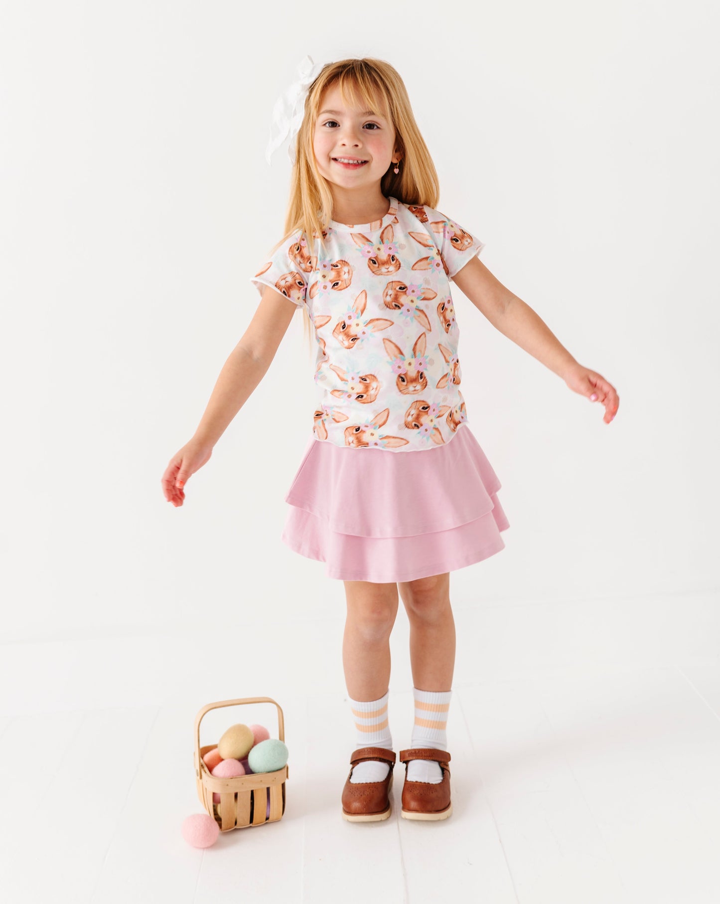 Young girl in a floral top and pink skirt holding a basket of Easter eggs on a white background
