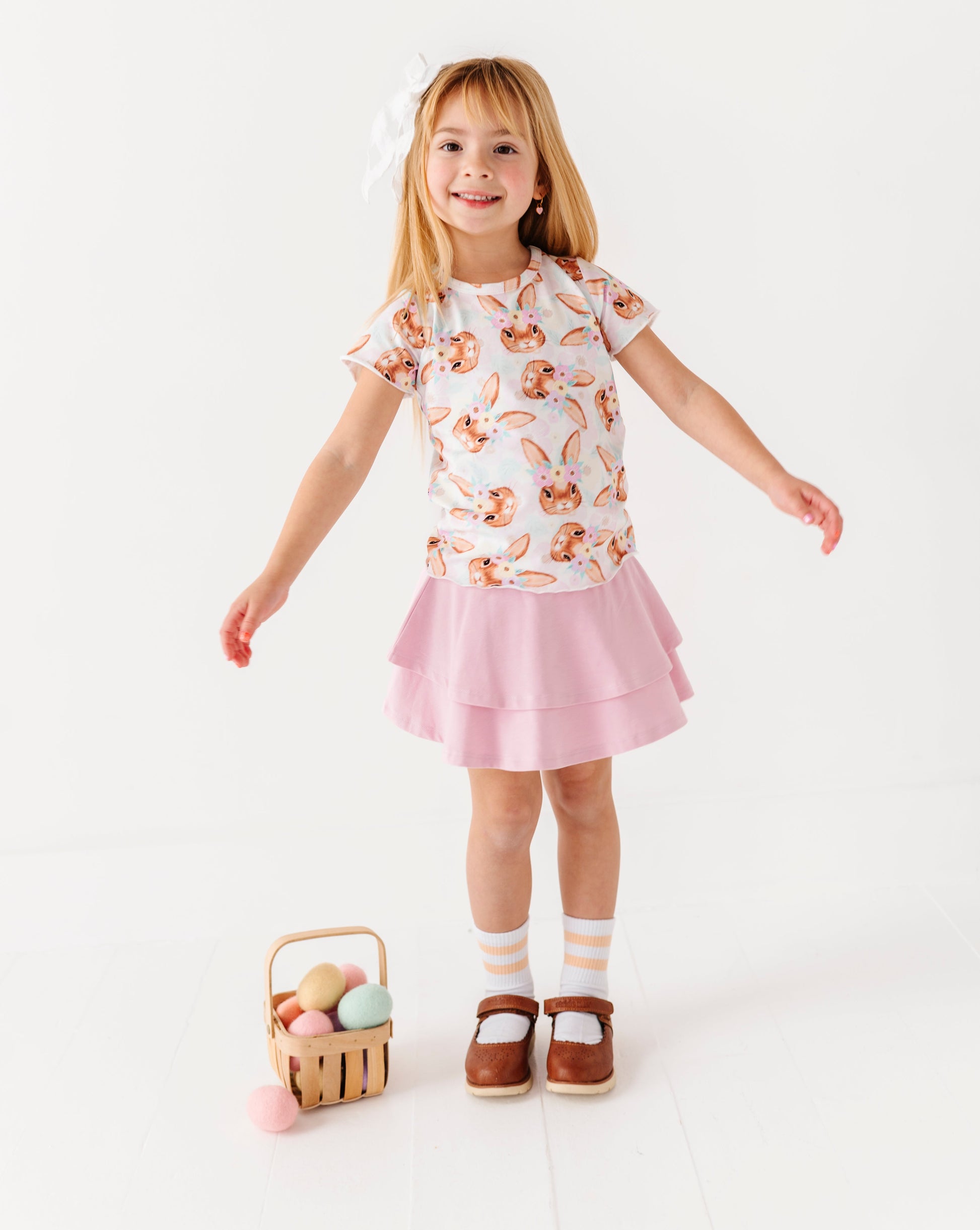 Young girl in a floral top and pink skirt holding a basket of Easter eggs on a white background