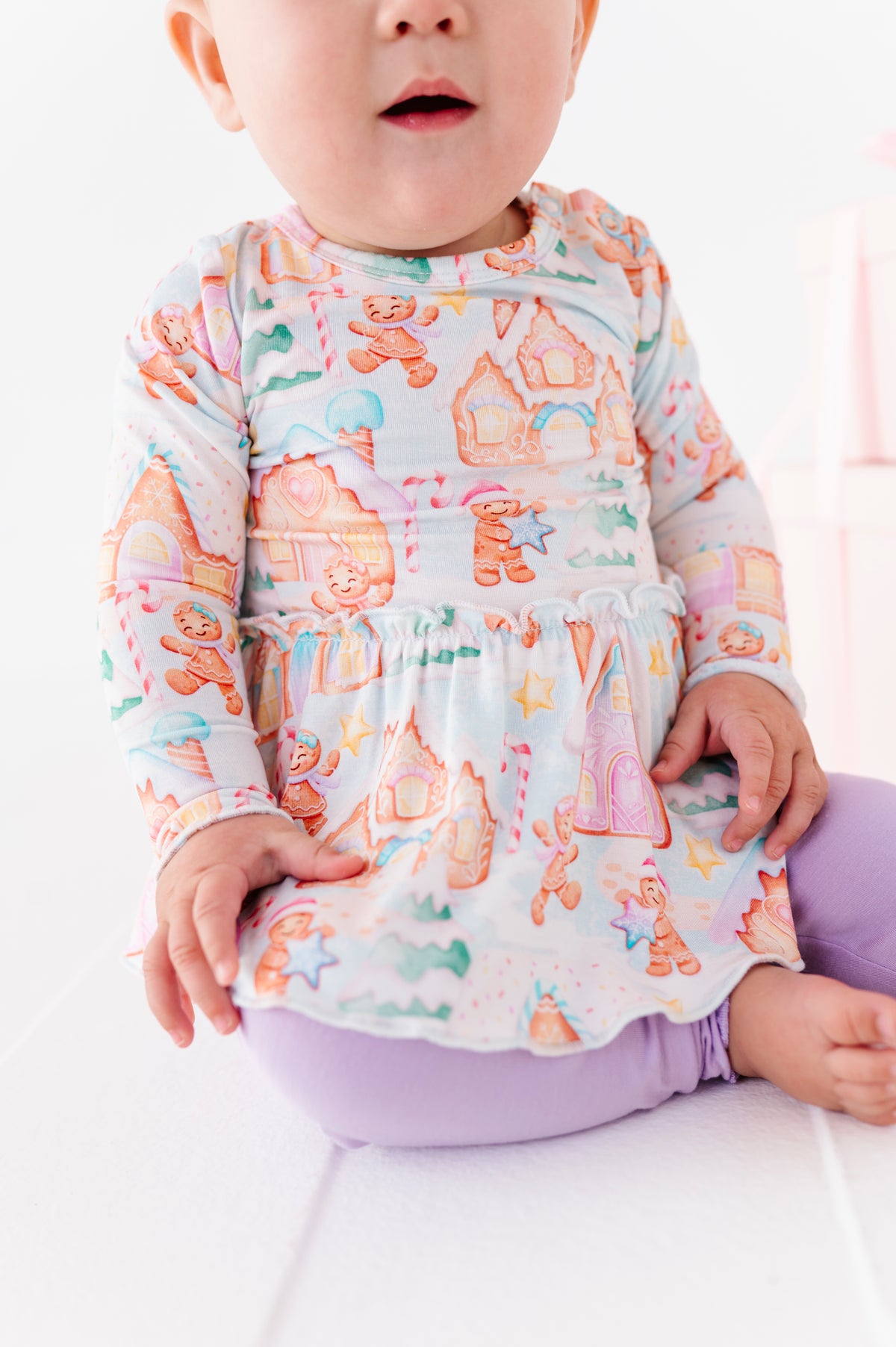 A baby girl wearing a Christmas gingerbread village-themed bamboo peplum with light purple bamboo leggings