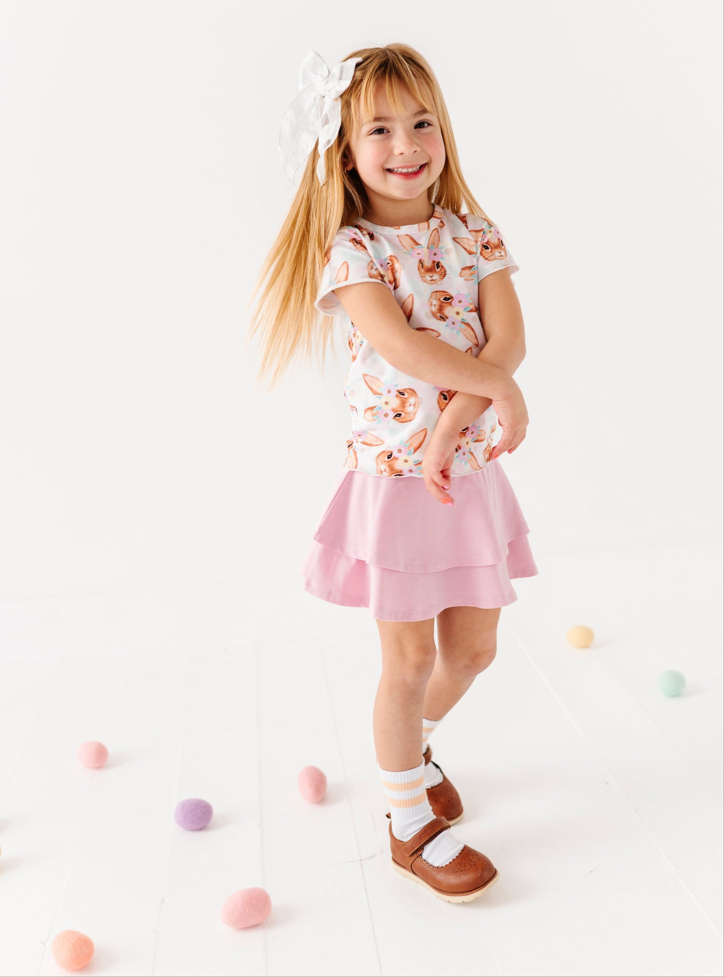 Young girl in a floral top and pink skirt standing on a white background with colorful balls.