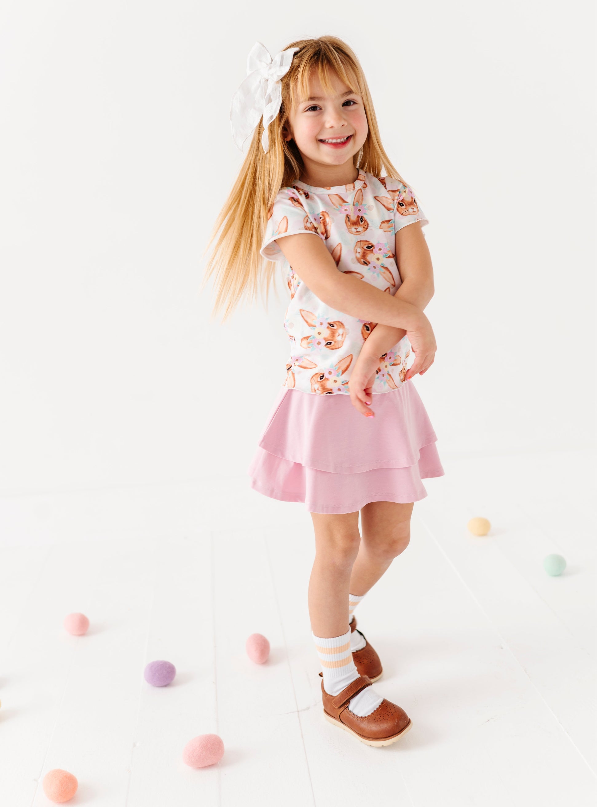 Young girl in a floral top and pink skirt standing on a white background with colorful balls.