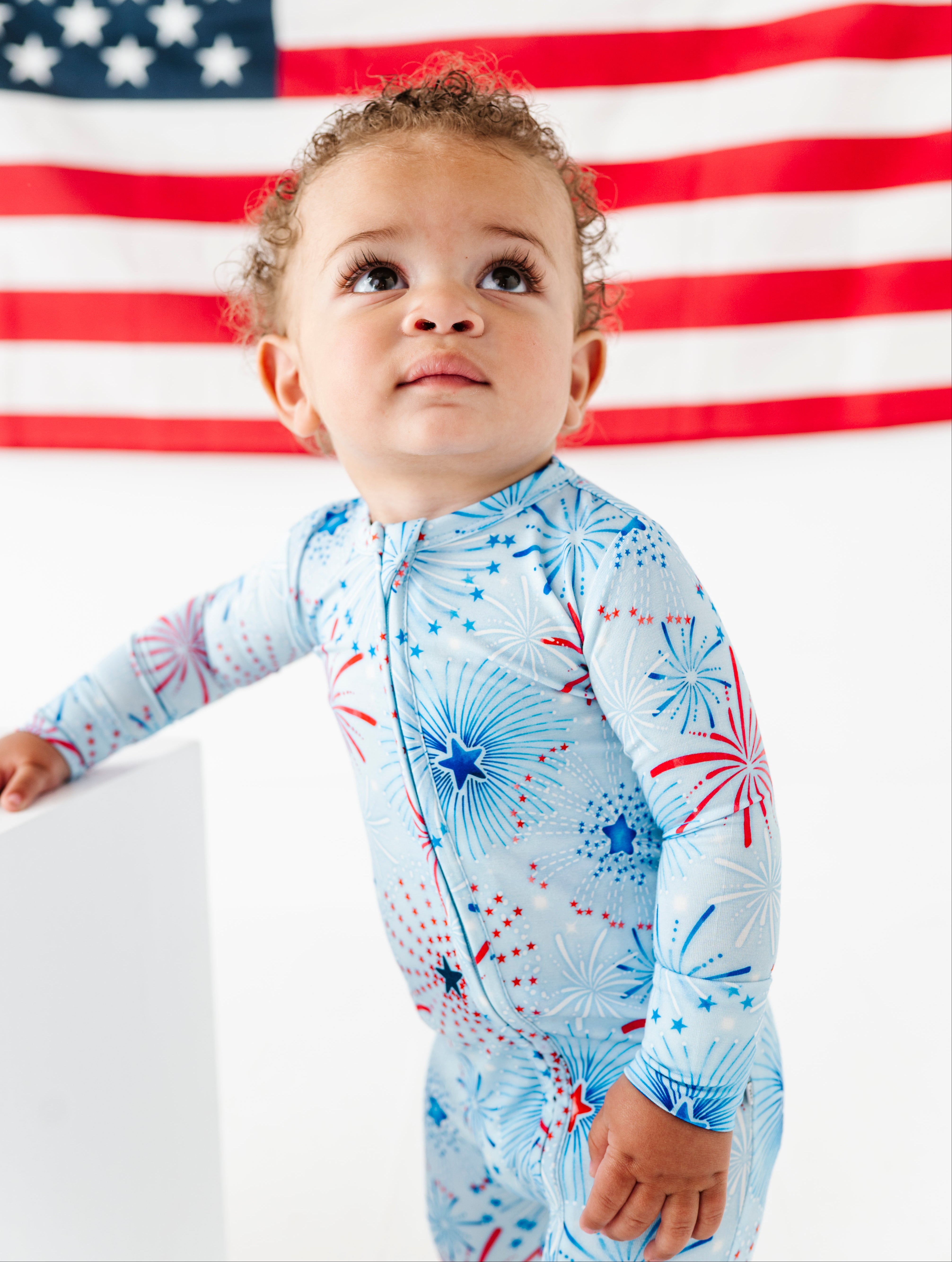 Baby wearing a blue firework-patterned bamboo onesie in front of an American flag