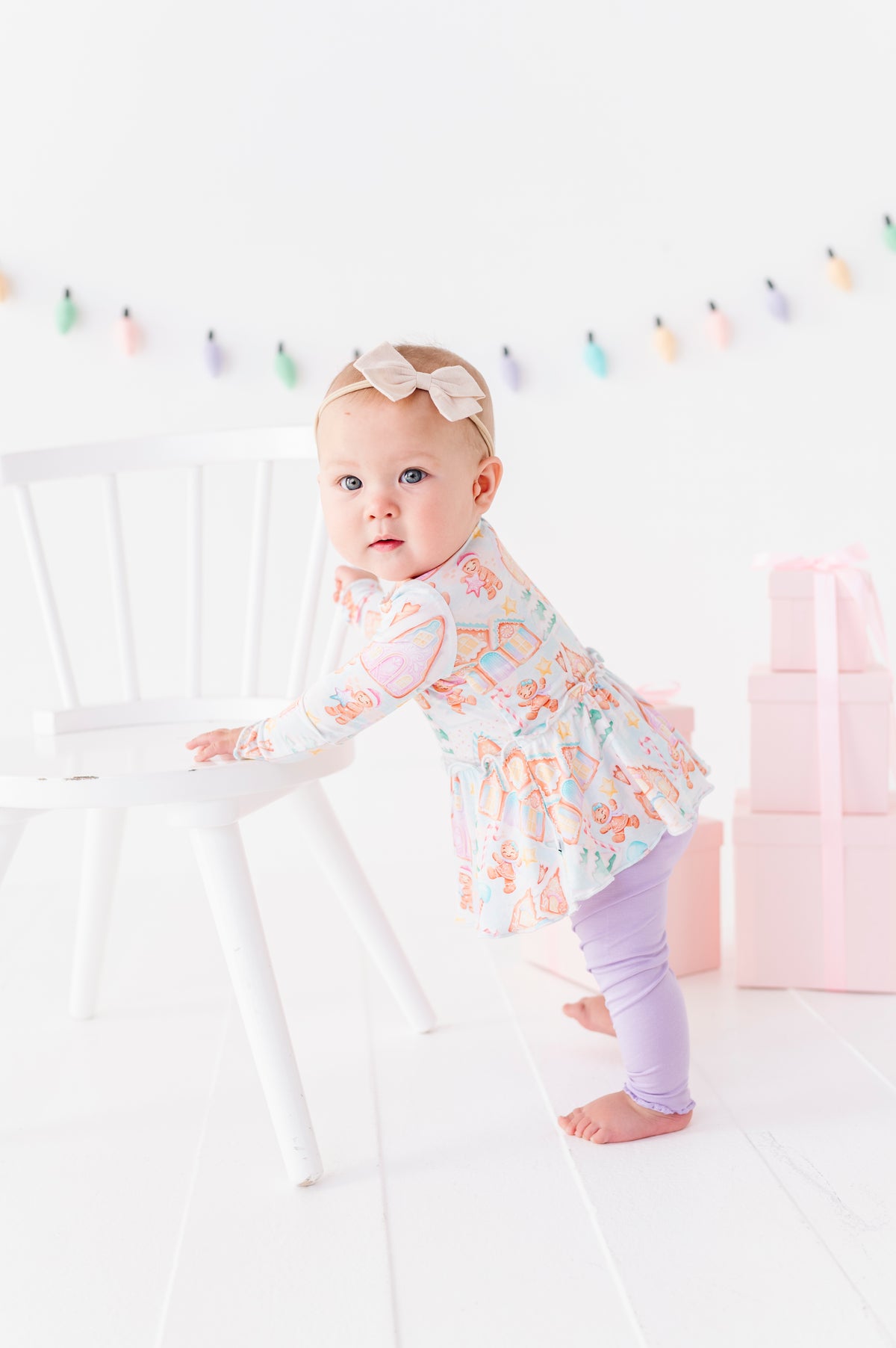 A baby girl wearing a Christmas gingerbread village-themed bamboo peplum with light purple bamboo leggings