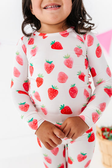 Child wearing a strawberry-patterned pajama set on a white background