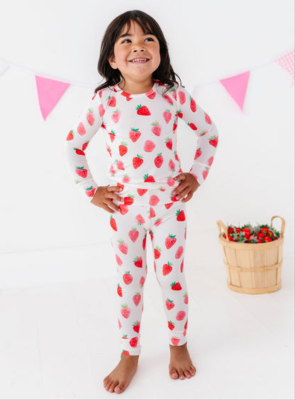 Child wearing strawberry-patterned pajamas with a basket of strawberries on a white background