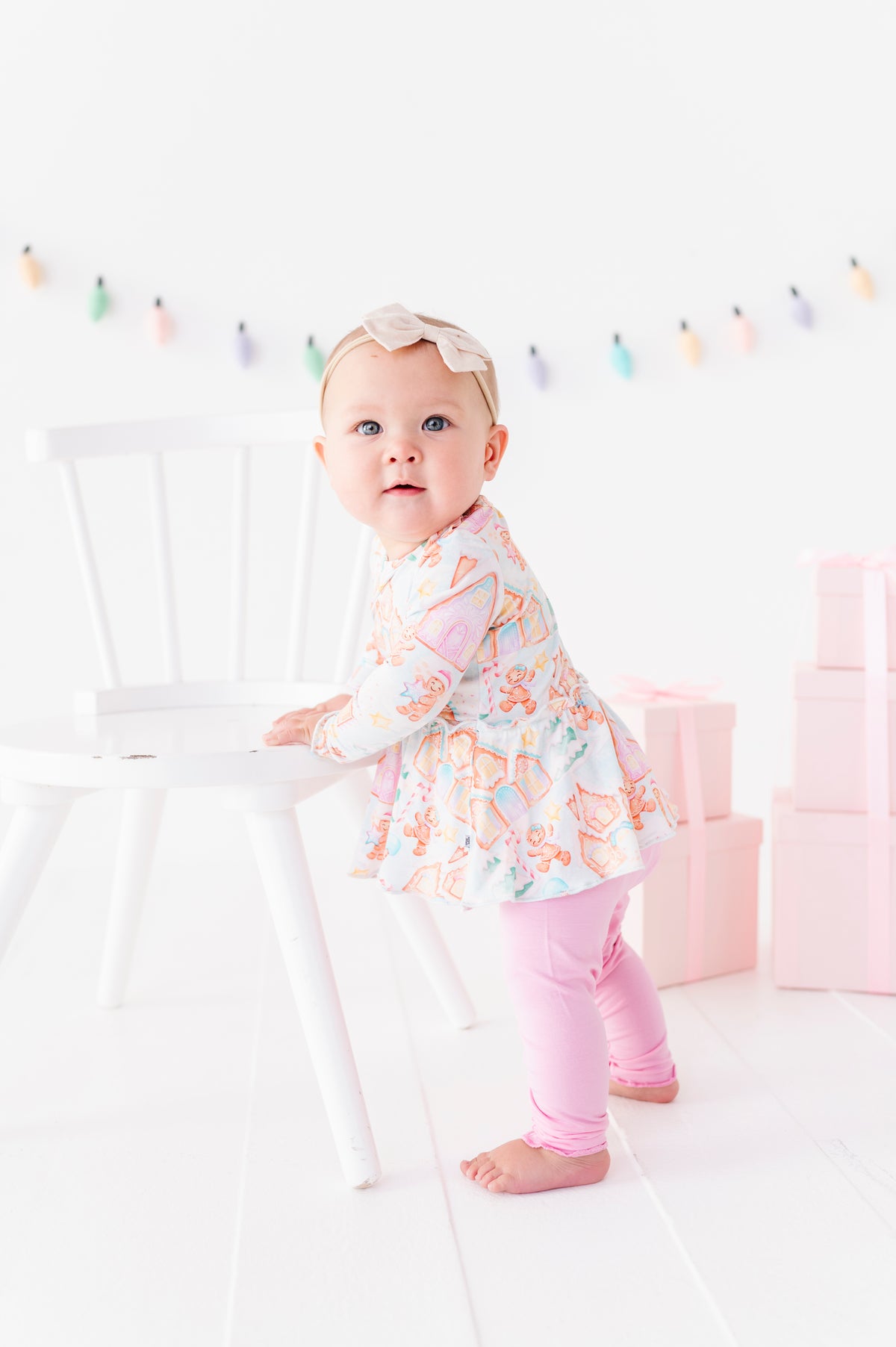 A baby girl wearing a Christmas gingerbread village-themed bamboo peplum with light purple bamboo leggings