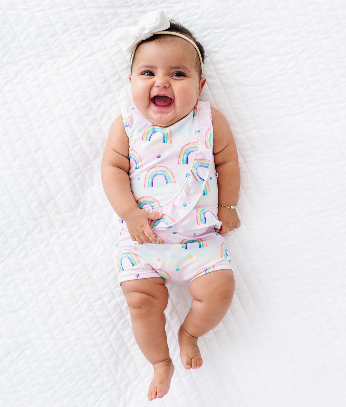 Baby wearing a rainbow-patterned bamboo cotton outfit lying on a white surface