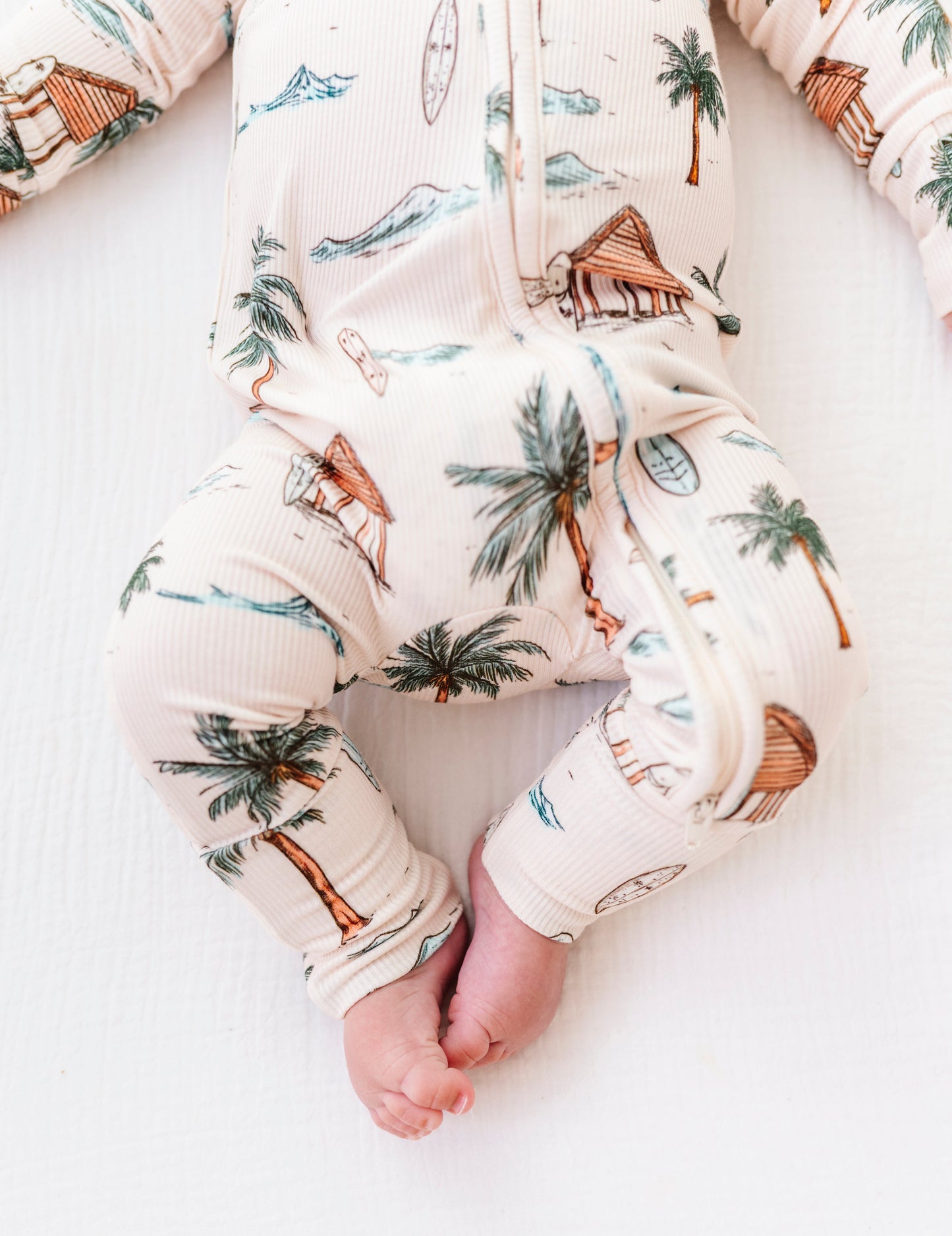 Baby's legs wearing a romper with palm tree and beach print on a white background