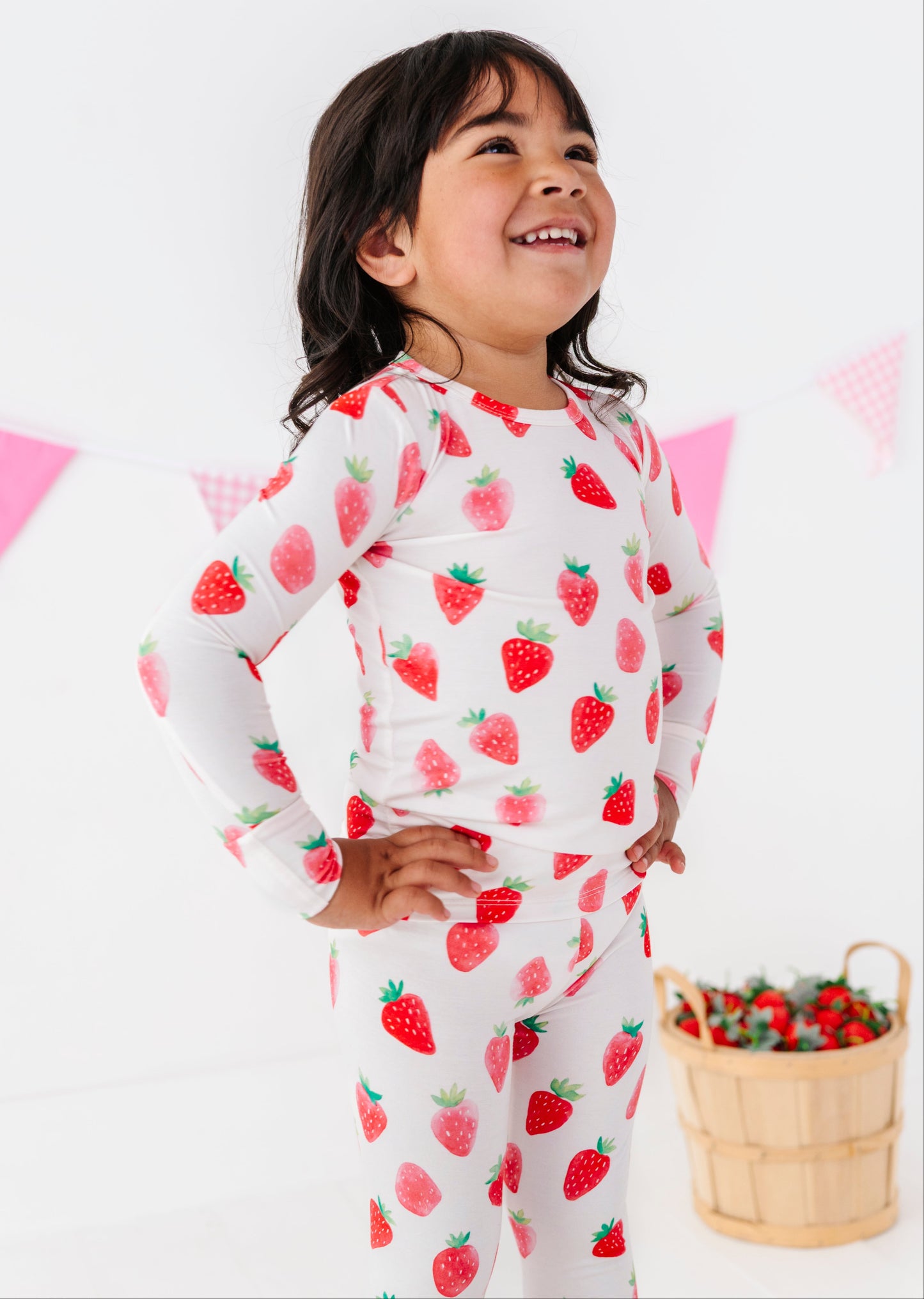 Child wearing strawberry-patterned pajamas with a basket of strawberries on a white background