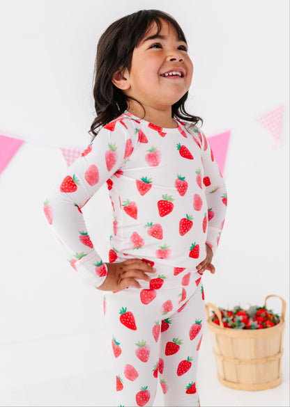 Child wearing strawberry-patterned pajamas with a basket of strawberries on a white background