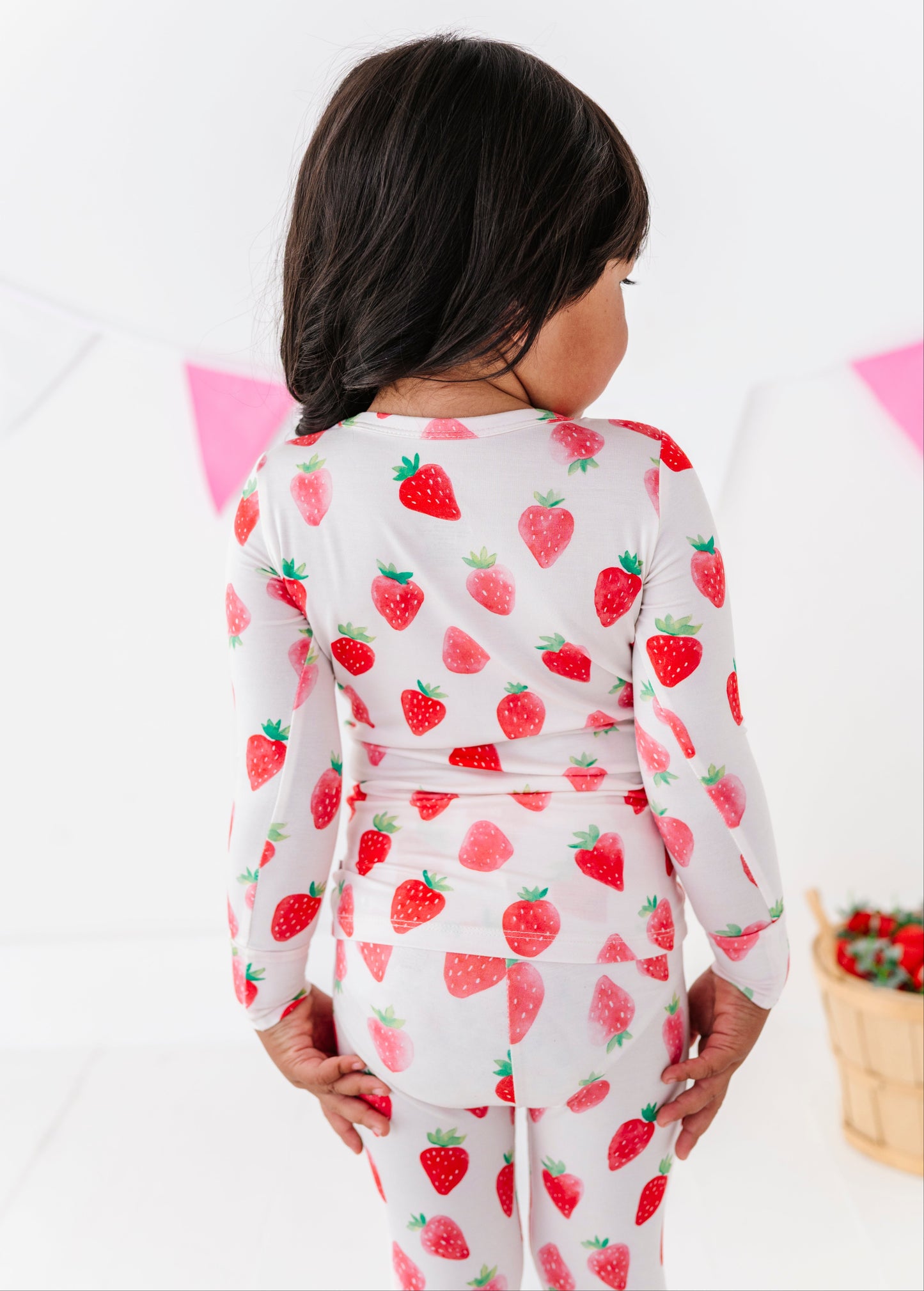 Child wearing strawberry-patterned pajamas against a white background