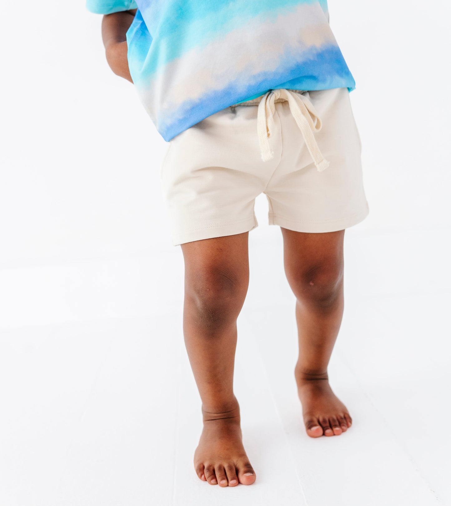 Little boy wearing a tie-dye bamboo shirt and beige bamboo-cotton shorts on a white background