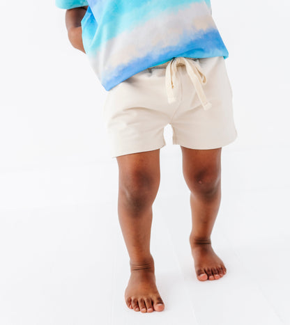 Little boy wearing a tie-dye bamboo shirt and beige bamboo-cotton shorts on a white background