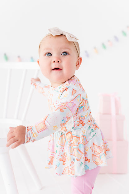 A baby girl wearing a Christmas gingerbread village-themed bamboo peplum with light purple bamboo leggings