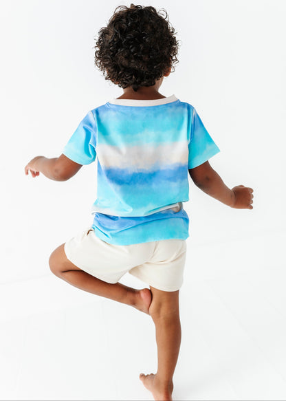 Child wearing a blue tie-dye shirt and ivory bamboo shorts on a white background