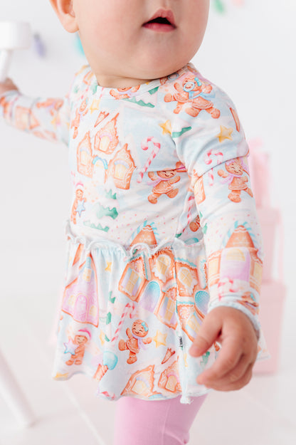 A baby girl wearing a Christmas gingerbread village-themed bamboo peplum with light pink bamboo leggings
