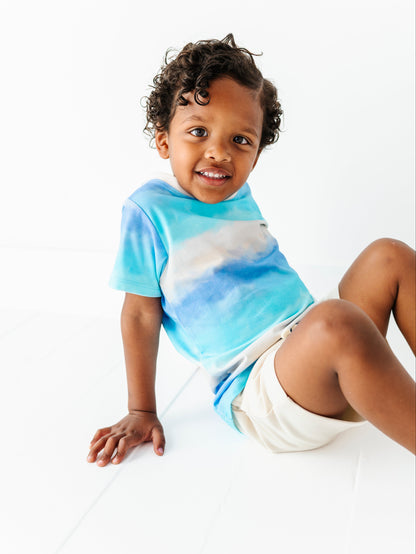 Child wearing a blue ombre shirt paired with ivory bamboo-cotton shorts on a white background