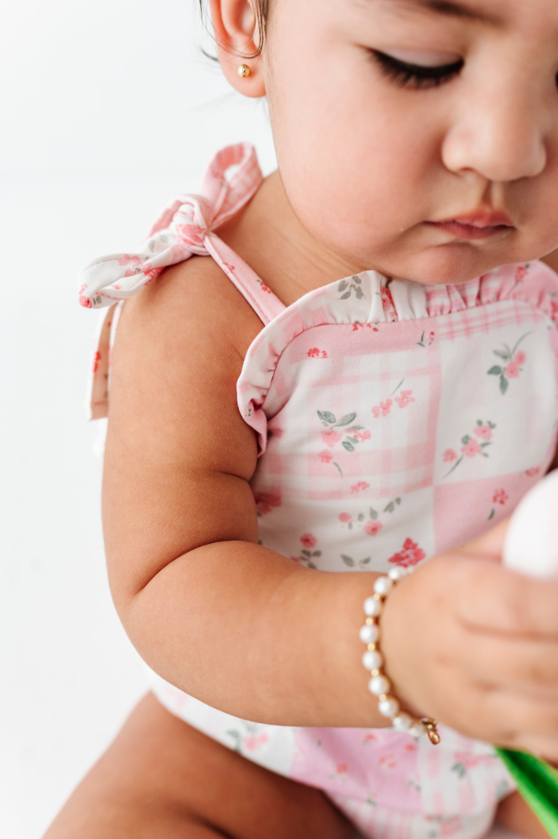 Baby girl in a floral bamboo bubble romper holding a flower on a white background