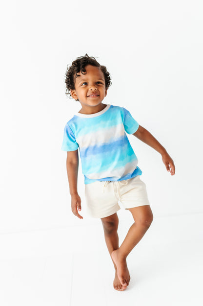 Child wearing a blue tie-dye bamboo-cotton shirt and ivory shorts on a white background